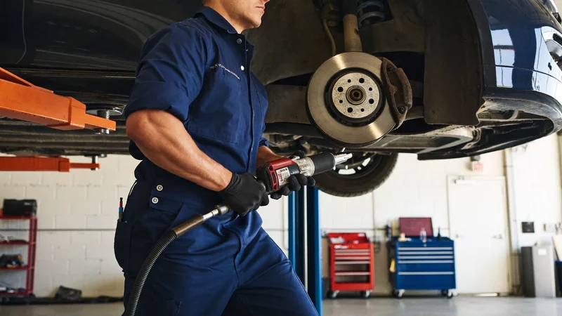 Mechanik sundává kolo ze zvednutého auta pneumatickým utahovákem